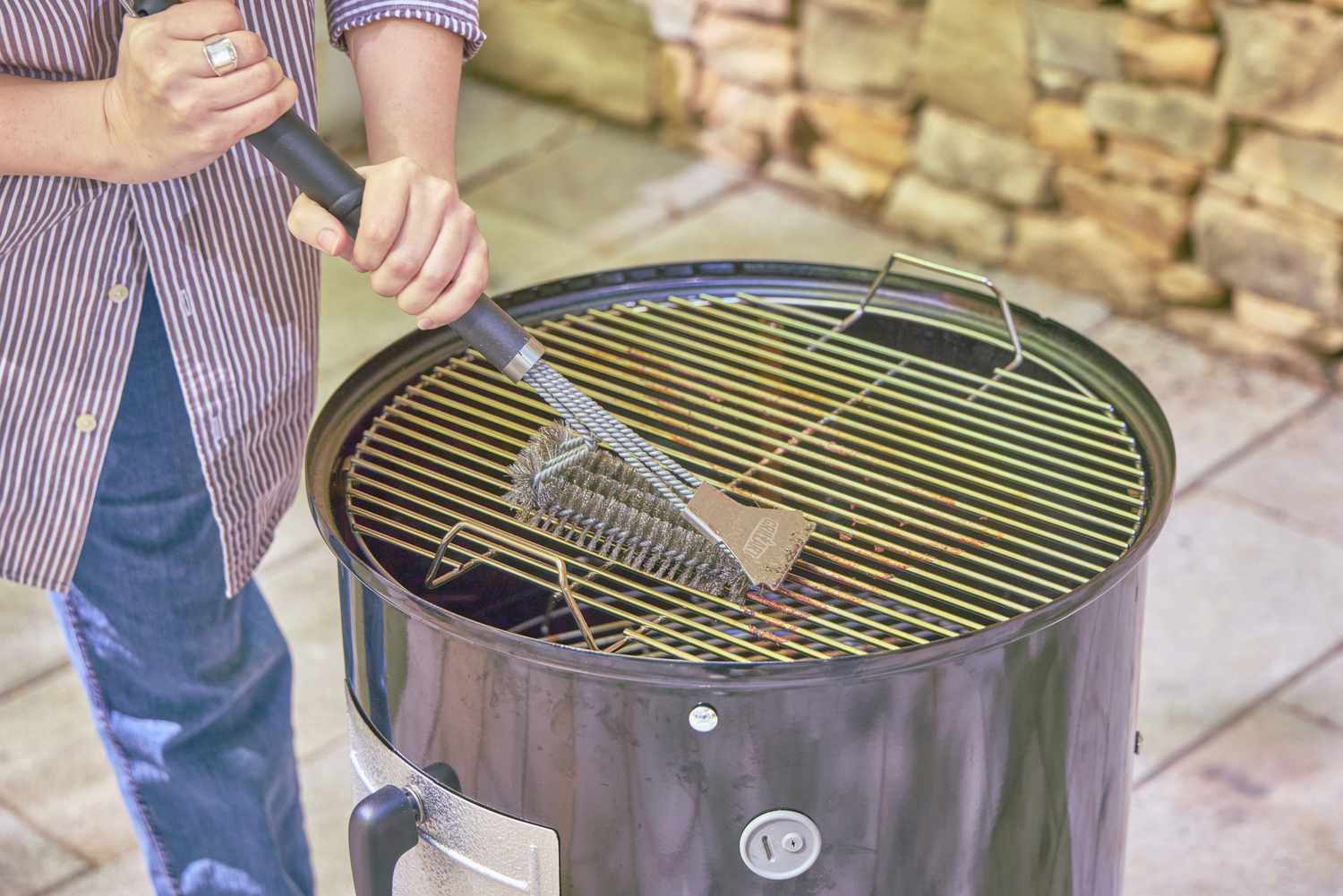 A person cleans the grate on the Weber 18-Inch Smokey Mountain Cooker