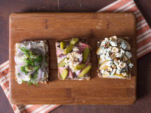 Three different Smørrebrød on a wood cutting board, each with different toppings.