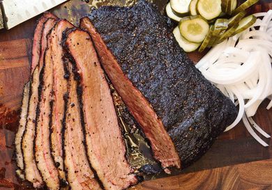 Cooked, sliced sous vide brisket on a cutting board with thinly sliced onions and pickles. 