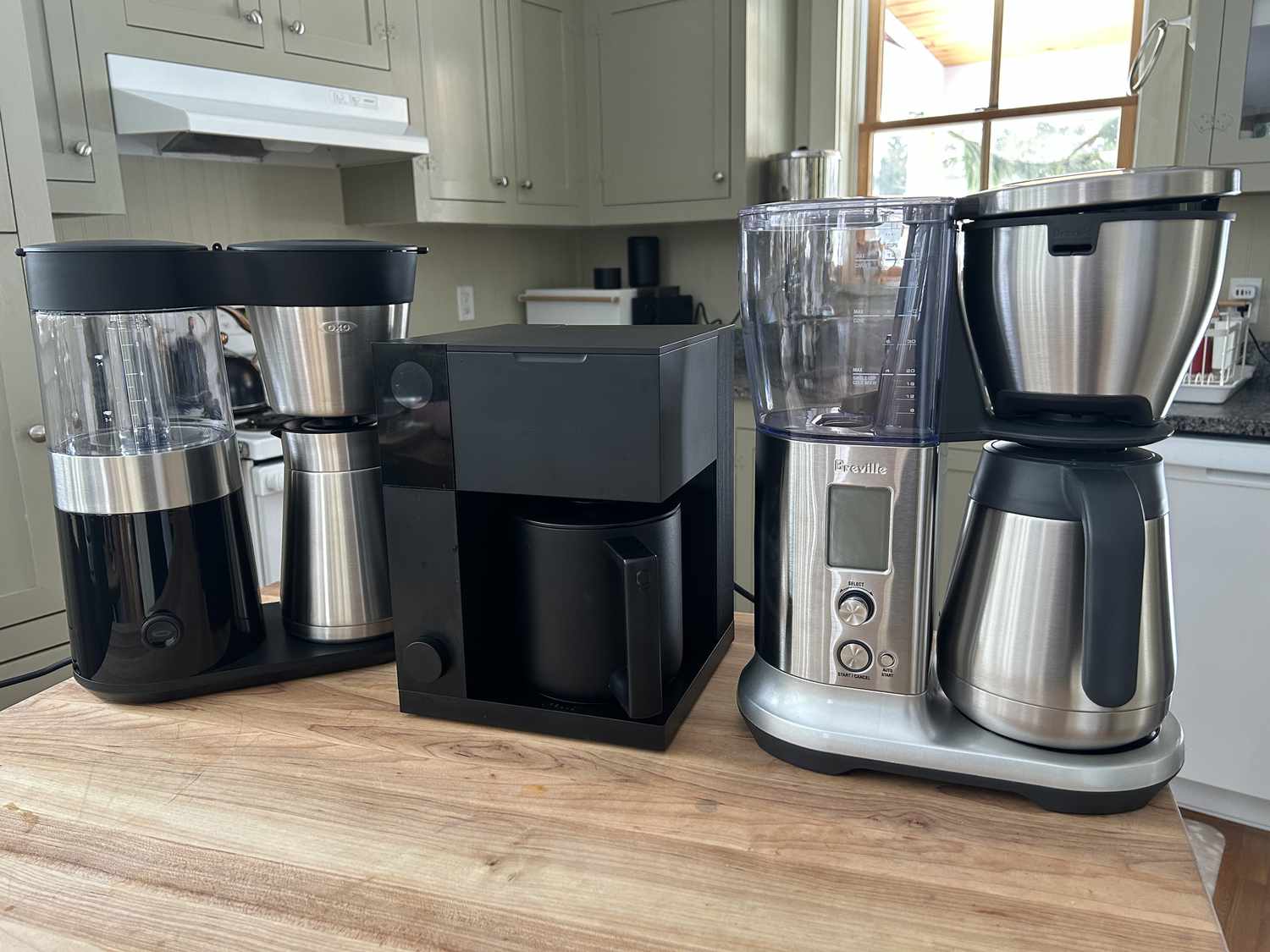 Three coffee makers sitting on a wooden table in a kitchen