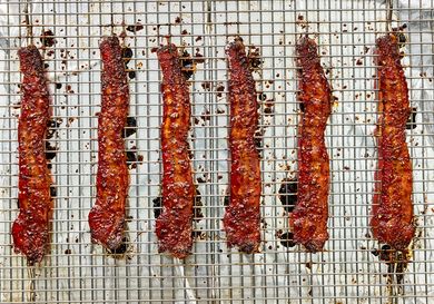 Six strips of seasoned bacon on a wire rack for cooking