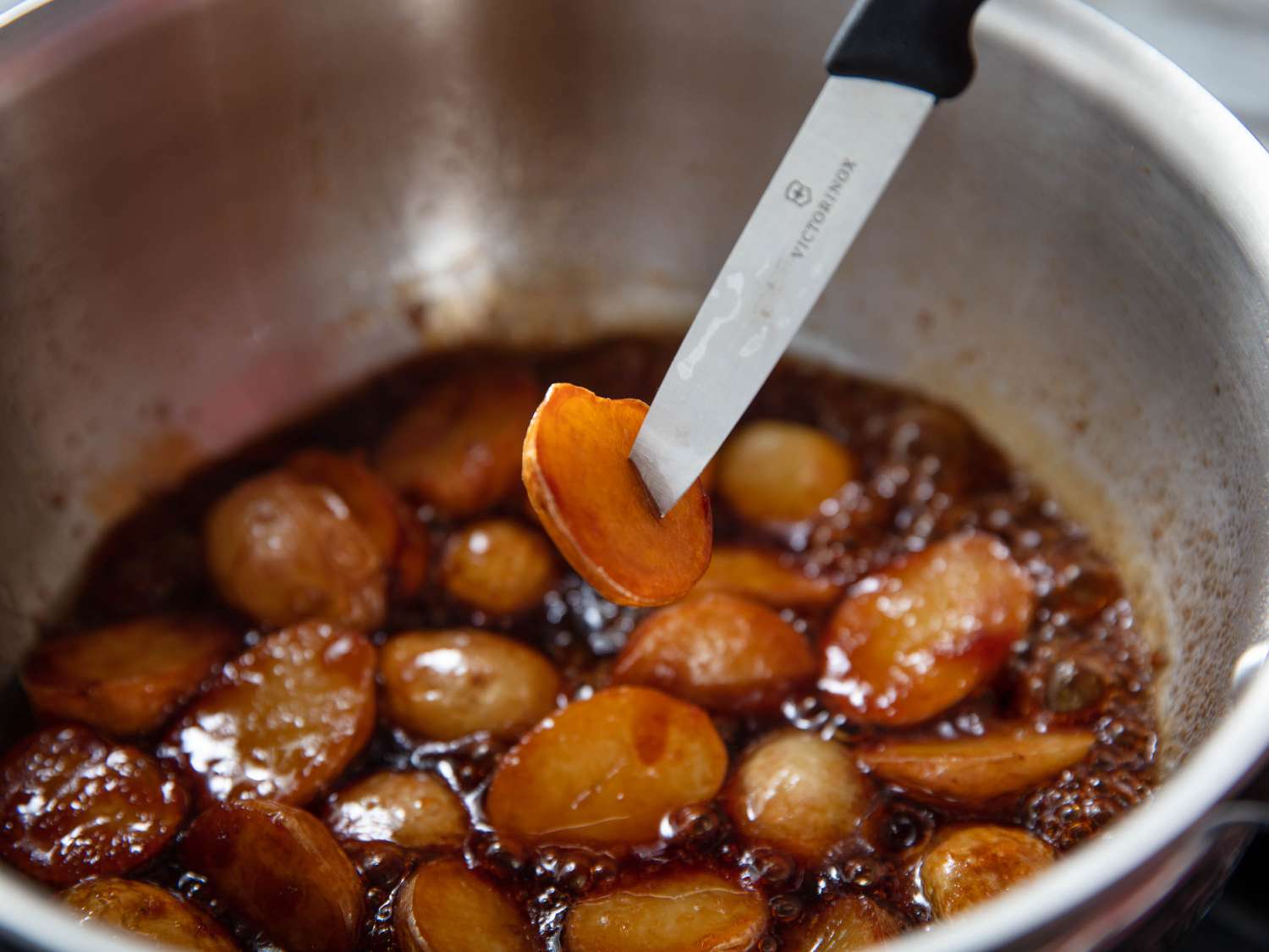 Simmering potatoes in soy sauce mixture, and testing for doneness with a paring knife.