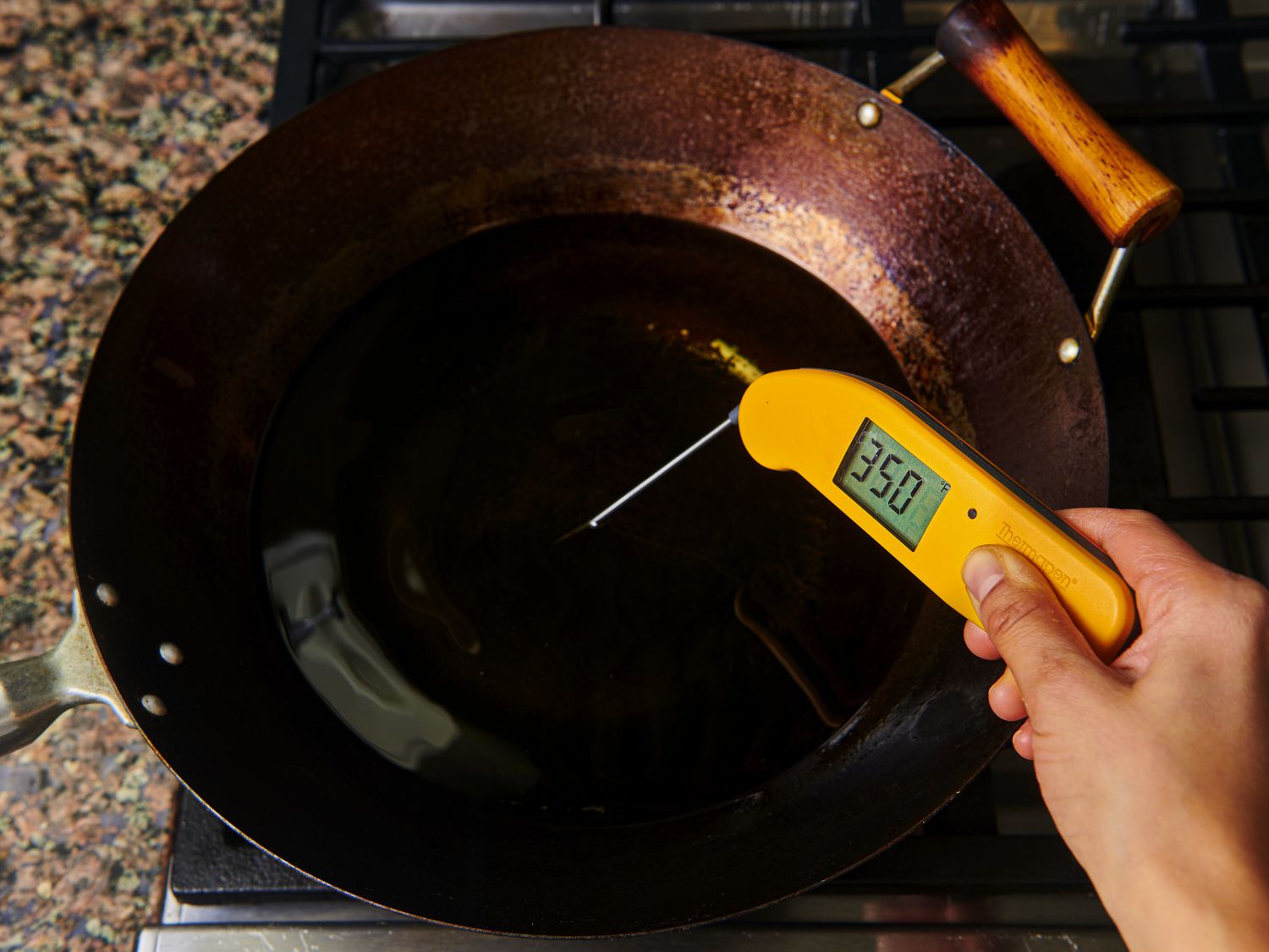 1 Â½ quarts of oil heating to 350Â°F in a large carbon steel wok. There is a hand holding an instant read thermometer which is inserted into the oil.