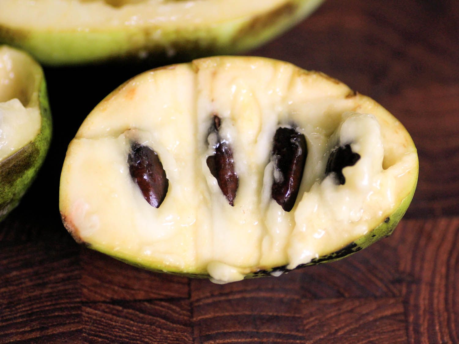 A pawpaw fruit cut in half and resting on a cutting board where you can see the seeds inside