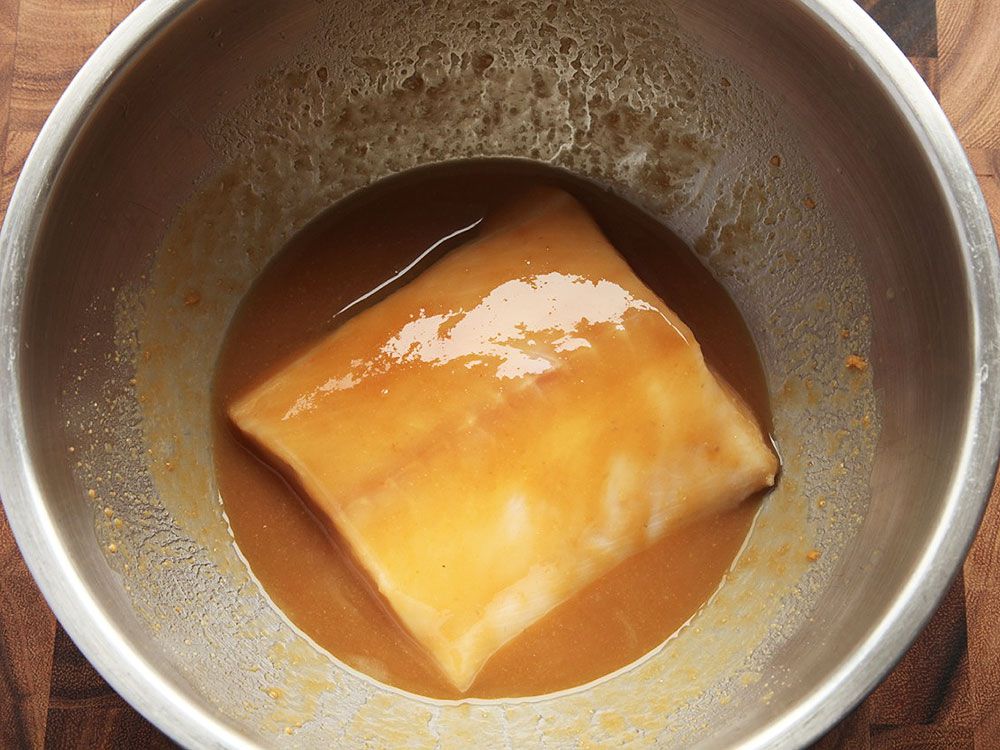 Overhead shot of a bowl of the sake-miso marinade. A black cod fillet is half-submerged in the bowl and coated with the marinade.