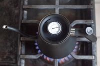 A gooseneck stovetop kettle with a thermometer dial placed on a lit gas burner