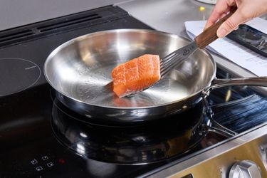 Cooking salmon in a stainless steel frying pan on an electric stovetop
