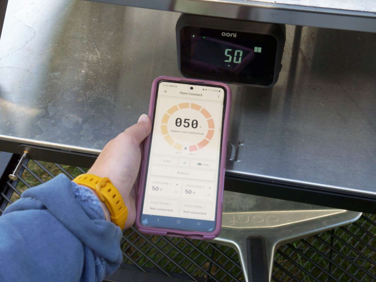 a person holding their phone with the app open in front of the ooni temperature display with 