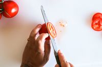 Hands slicing a tomato with a Material knife on a white surface