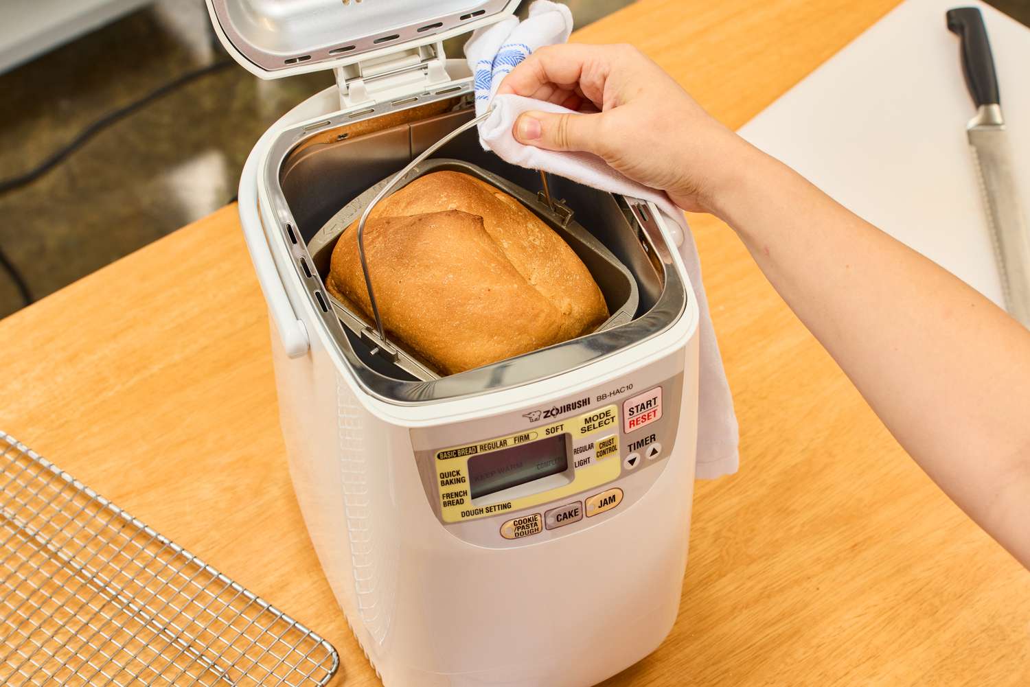 A hand using a towel to remove the bread basket from the Zojirushi Home Bakery Mini Breadmaker