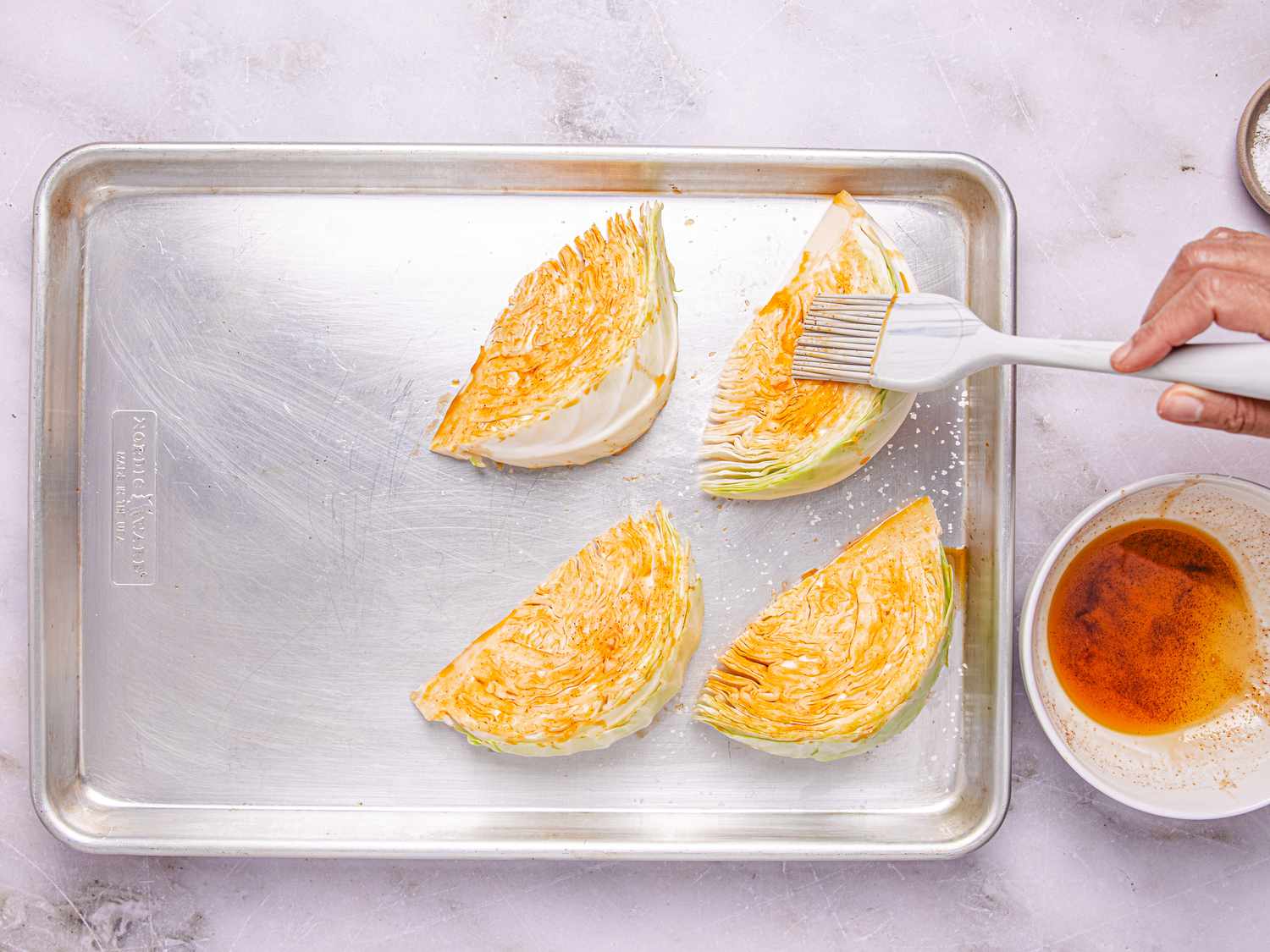 Cabbage wedges being brushed with seasoning on a baking sheet