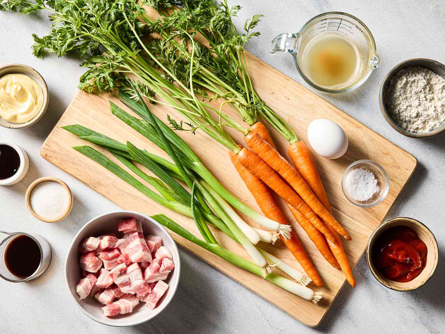 Ingredients on a wooden board including carrots, green onions, an egg, and bowls of mayonnaise, diced meat, flour