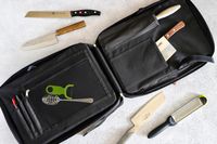 A knife and utensil carrying case with kitchen tools and knives laying nearby on the surface