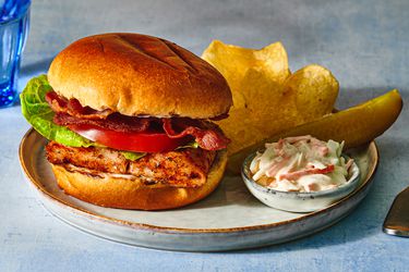 Grilled blackened-fish sandwich on a plate with potato chips, creamy coleslaw, and a pickle spear