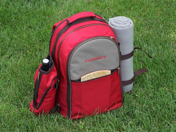 A red backpack picnic basket, with a wine bottle holder, a blanket, and a small cutting board. 