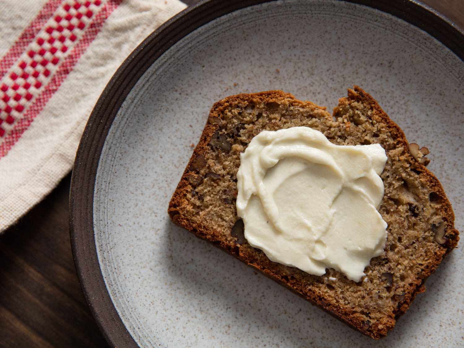 Slice of banana bread on a grey plate smeared with banana whipped cream.