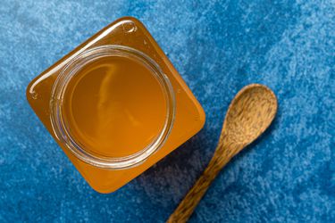 Overhead closeup of Clarified Butter in a square jar, set on a blue background.