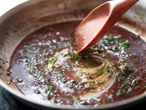 A broken pan sauce being stirred with a wooden spoon.