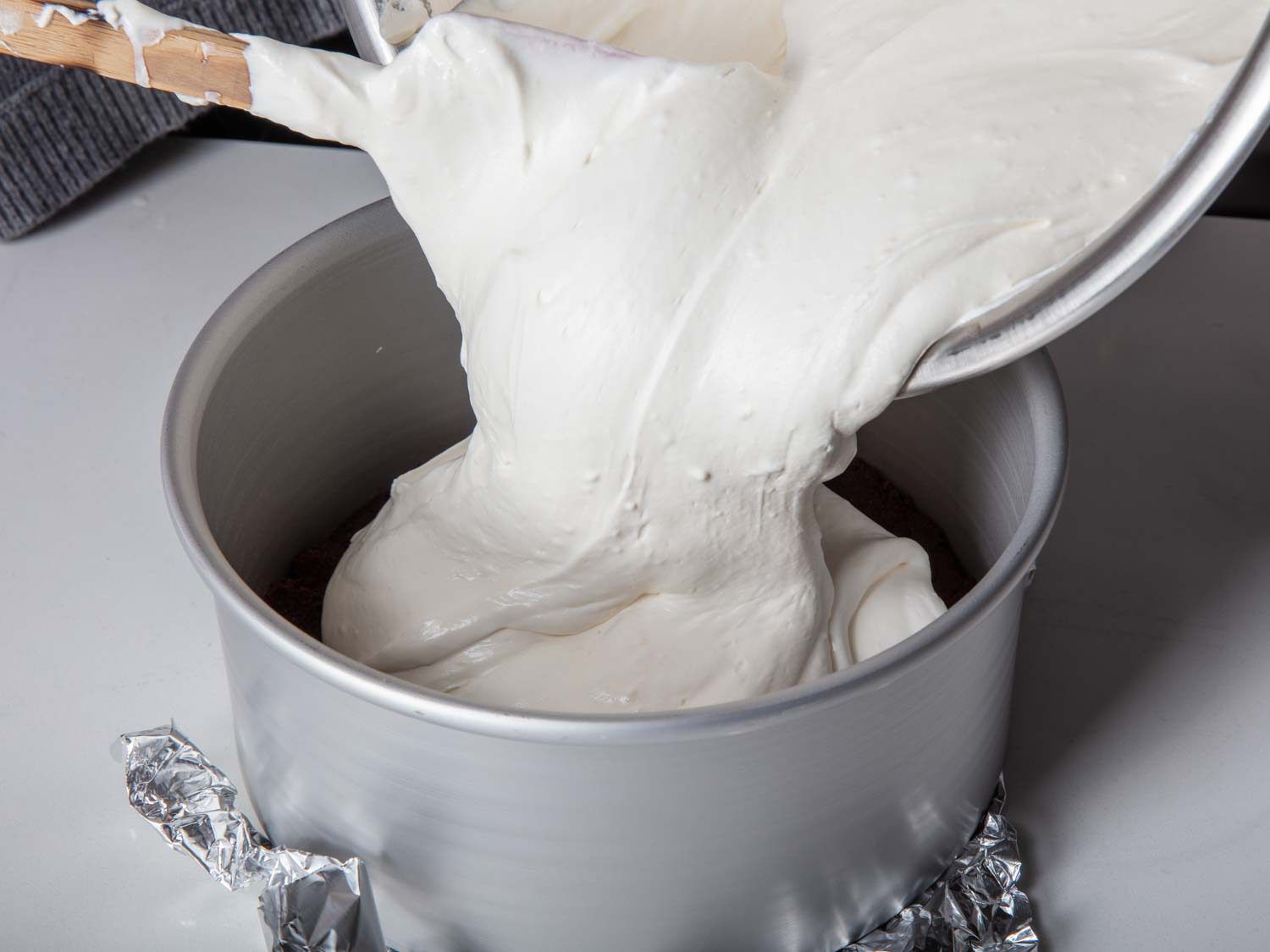 Transferring Greek yogurt cheesecake batter into a loose bottom pan lined with aluminium foil. 