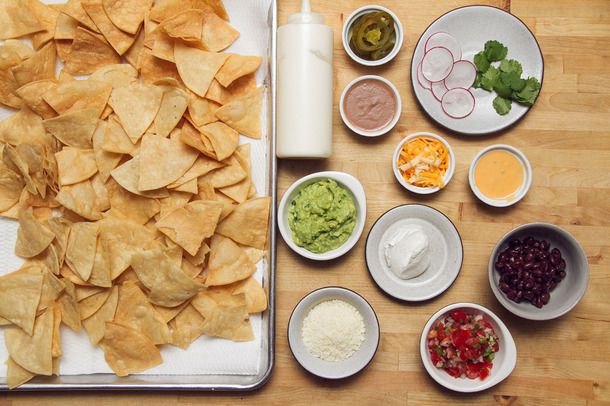 Overhead of bowls of toppings to be added to fully-loaded nachos.