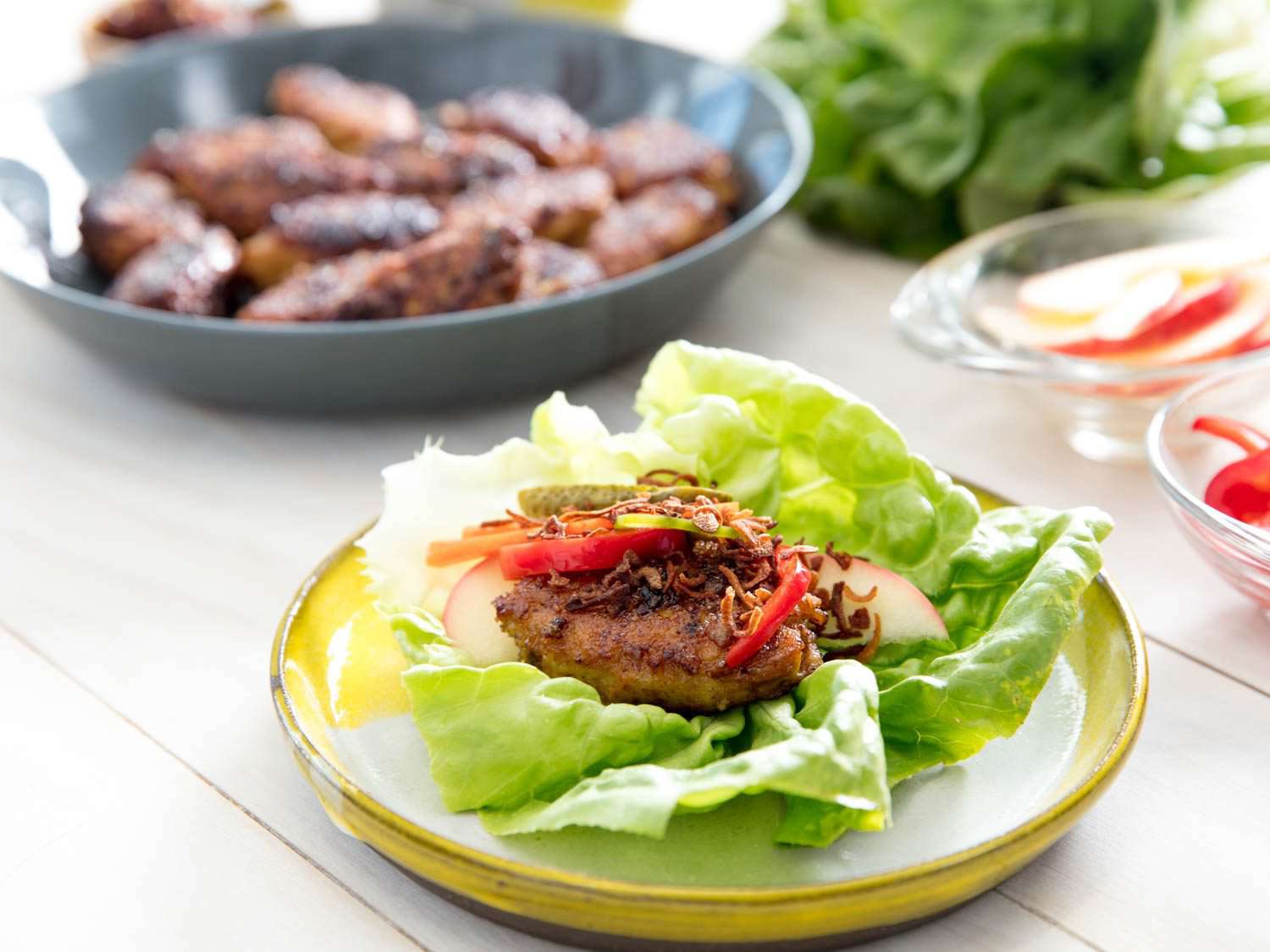 A Vietnamese-style chicken meatball is served on a lettuce leaf with pickles, sliced apple, and fried shallot.