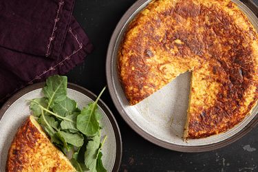 A tortilla Espaola sliced on a plate a serving with greens on the side