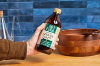A hand holding a bottle of Eden organic sesame oil above a wooden bowl on a countertop