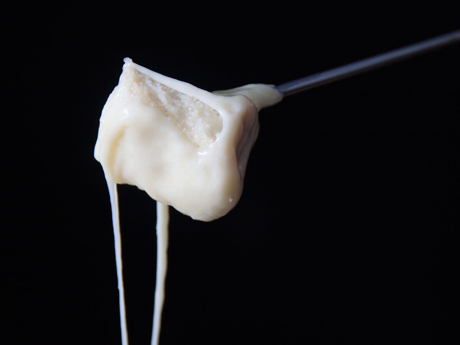 Cheese fondue on stick in front of black background.