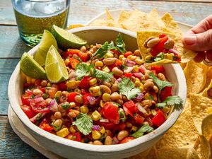 A bowl of cowboy caviar surrounded by tortilla chips with a hand holding a chip topped with the dish