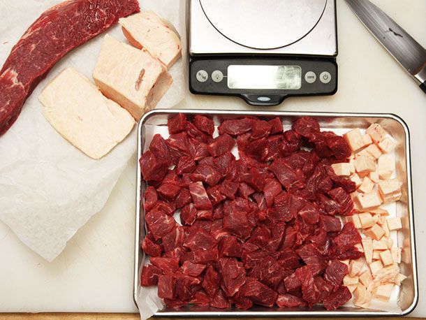 Lean cubed beef with cubes of beef suet on a rimmed baking sheet.