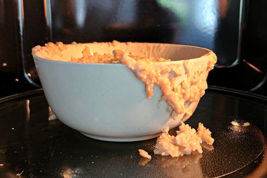 A bowl with spilled oatmeal placed on a microwave tray