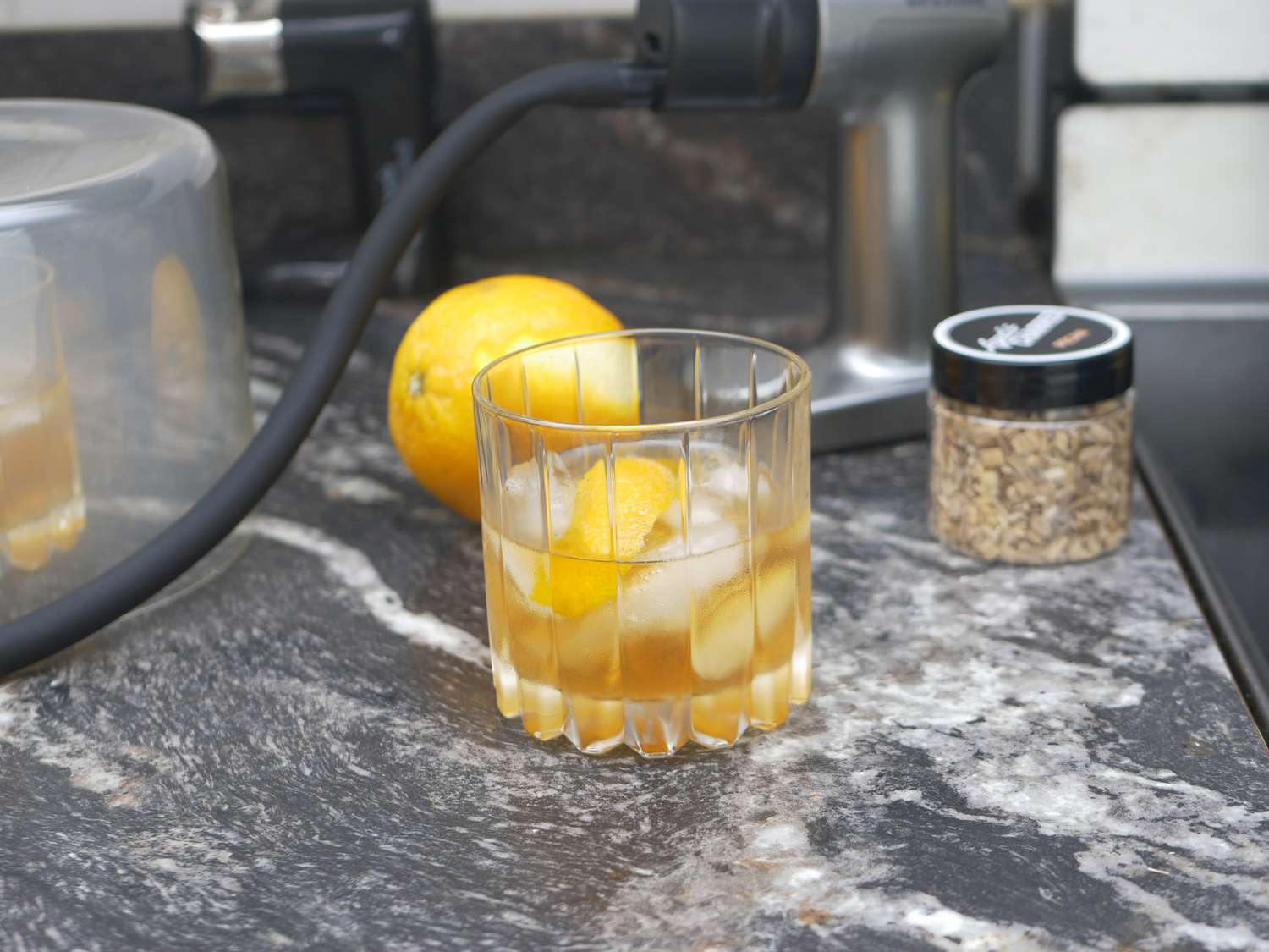 an old fashioned with a cocktail smoker behind it