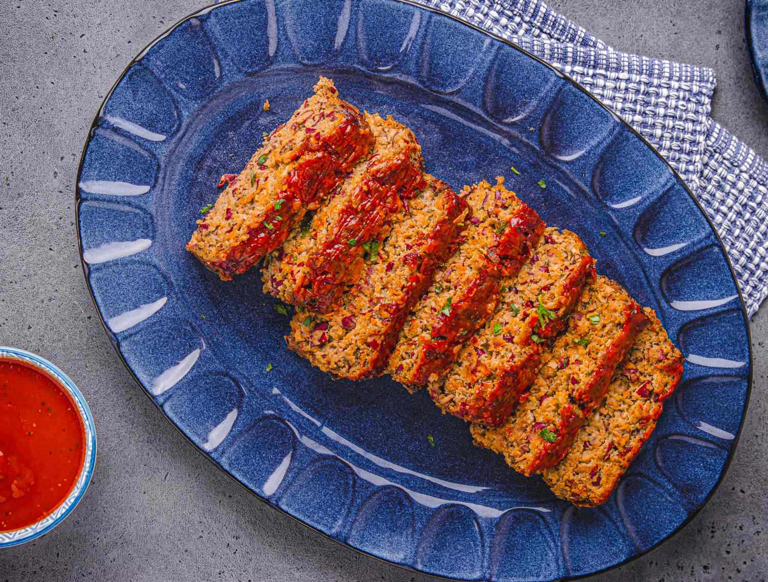 Slices of meatloaf arranged on a serving plate accompanied by a bowl of sauce beside it