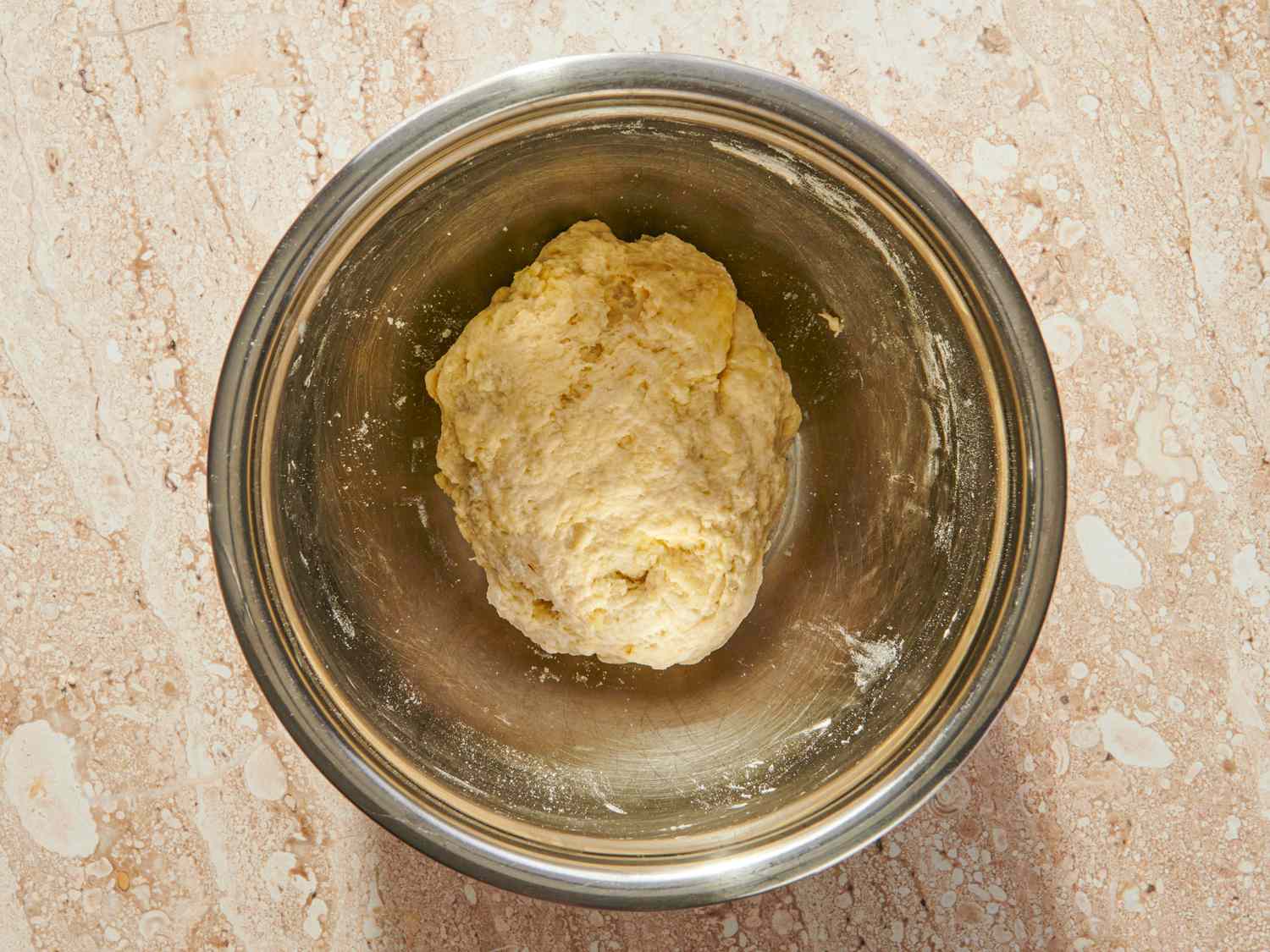 A metal bowl containing a mass of dough on a countertop