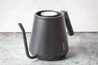 A metal kettle with a builtin thermometer on a textured surface