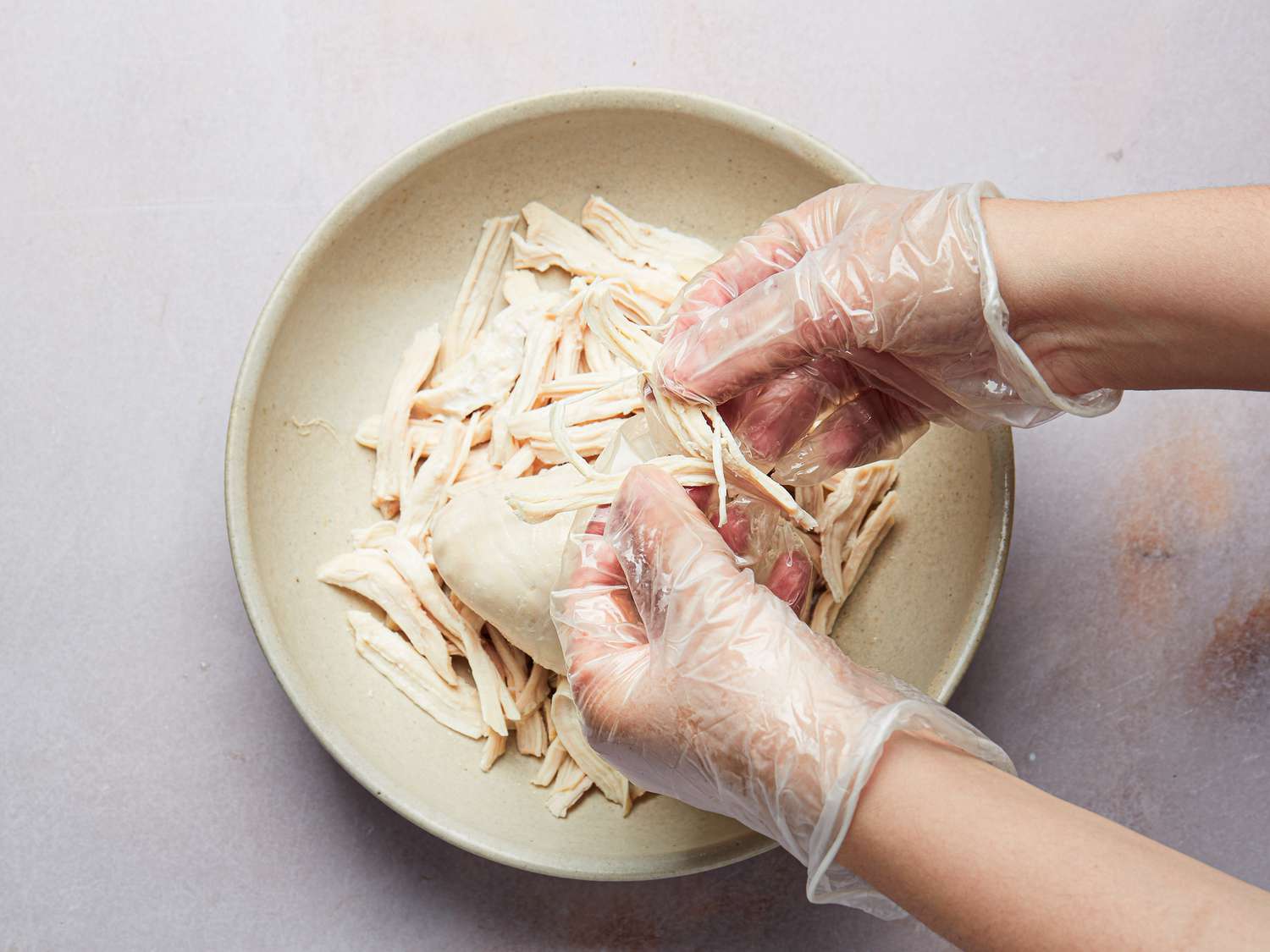 Overhead view of shredding chicken meat by hand
