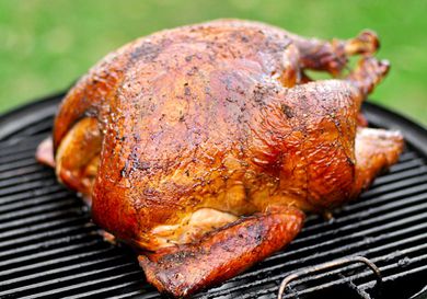 A golden Cajun-style turkey resting on the surface of a charcoal grill.