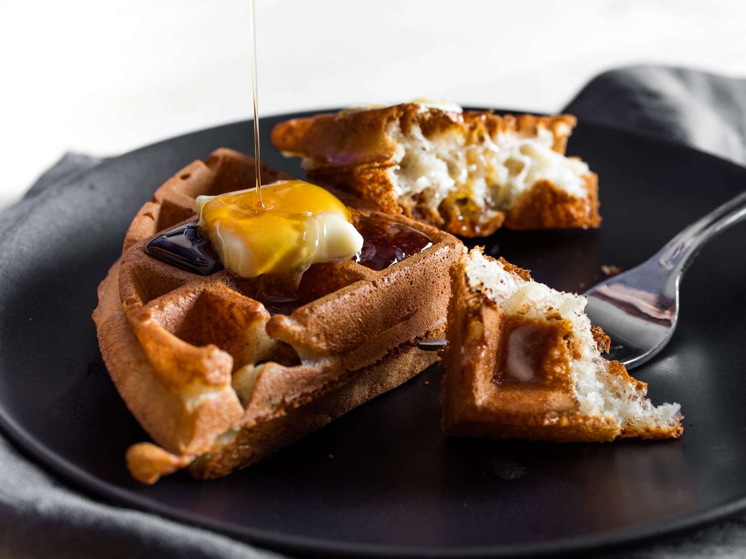 Drizzling syrup onto a waffle on a plate, topped with a pat of butter. 