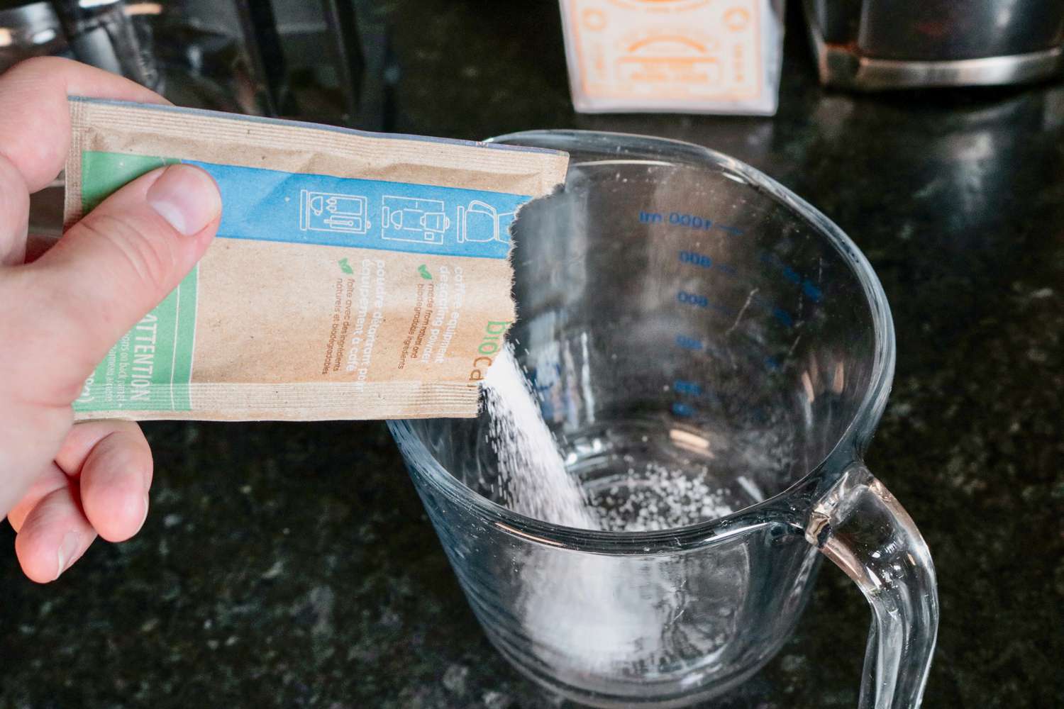 A hand pouring a packet of descaler into a glass liquid measuring cup
