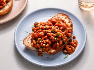 British-style baked beans on a piece of white bread which is placed on a blue ceramic plate on a stone background.