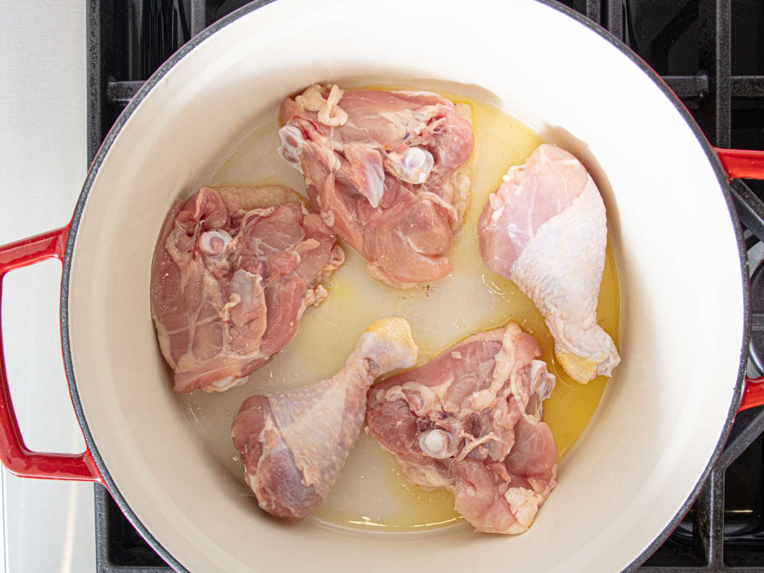 Raw chicken pieces in a pot with oil on a stovetop part of a cooking preparation process
