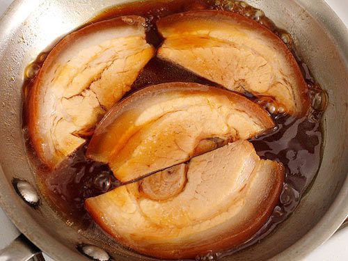 Slices of chashu pork being reheated in a skillet with the braising liquid.