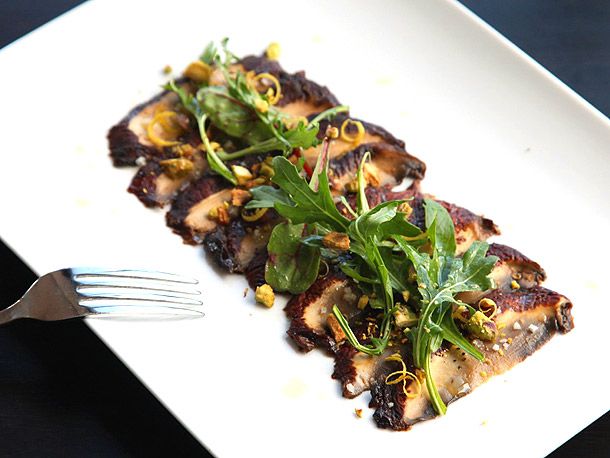 Miso-marinated portobello carpaccio served on a rectangular white plate, garnished with chopped pistachio, lemon zest, and arugula.