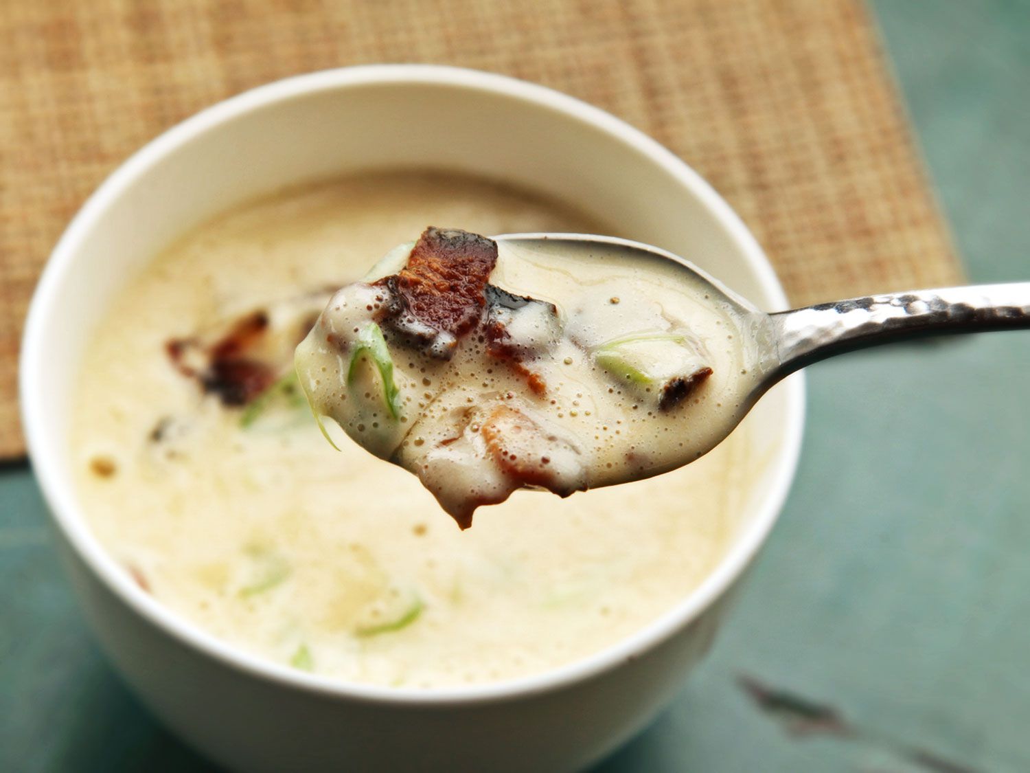 A spoonful of creamy cauliflower soup with bacon lifted from a white bowl
