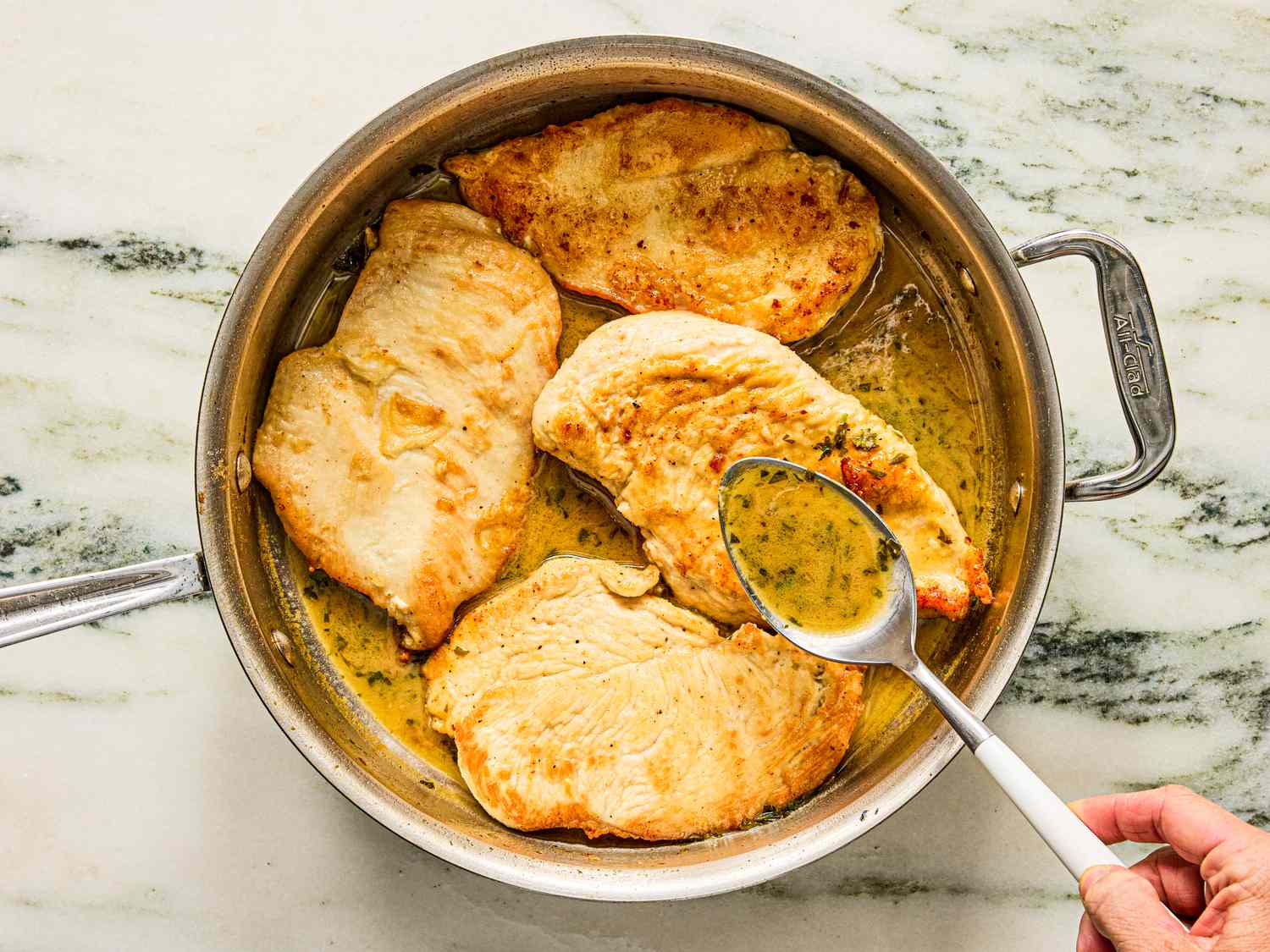 Pan with sautéed chicken breasts being basted in sauce
