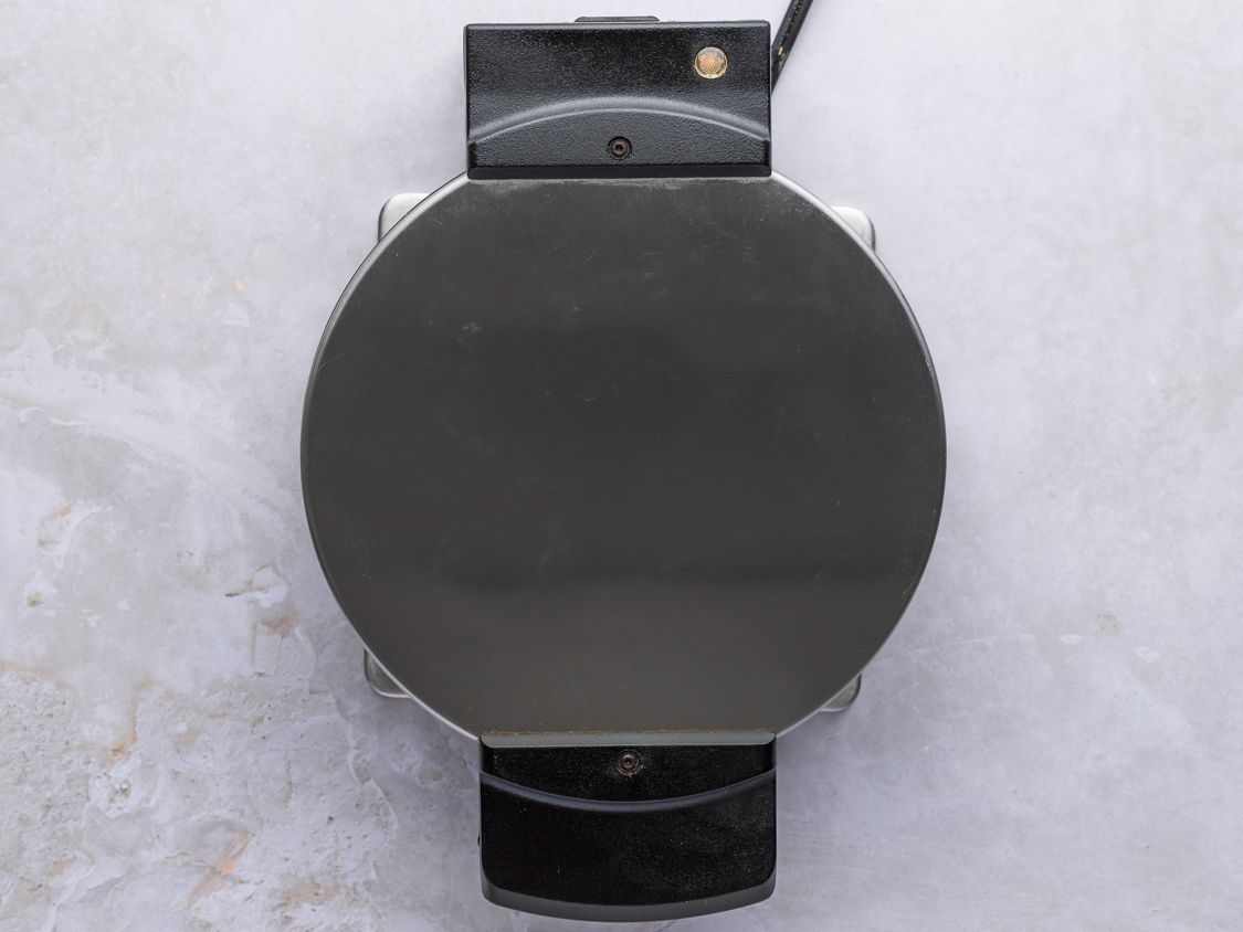 A closed waffle iron on a counter.