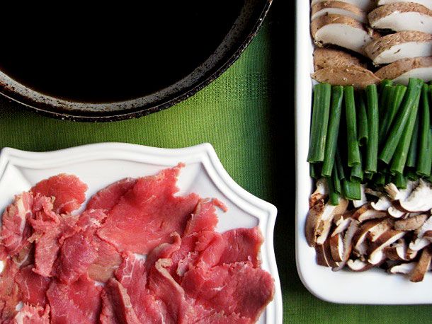 Overhead view of prepared meat and vegetables surrounding a pot for making sukiyaki.