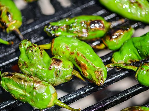 Closeup of Padrón peppers charring nicely on a grill grate.