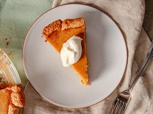 A slice of pumpkin pie topped with a dollop of whipped cream on a plate with a fork placed beside it on a table