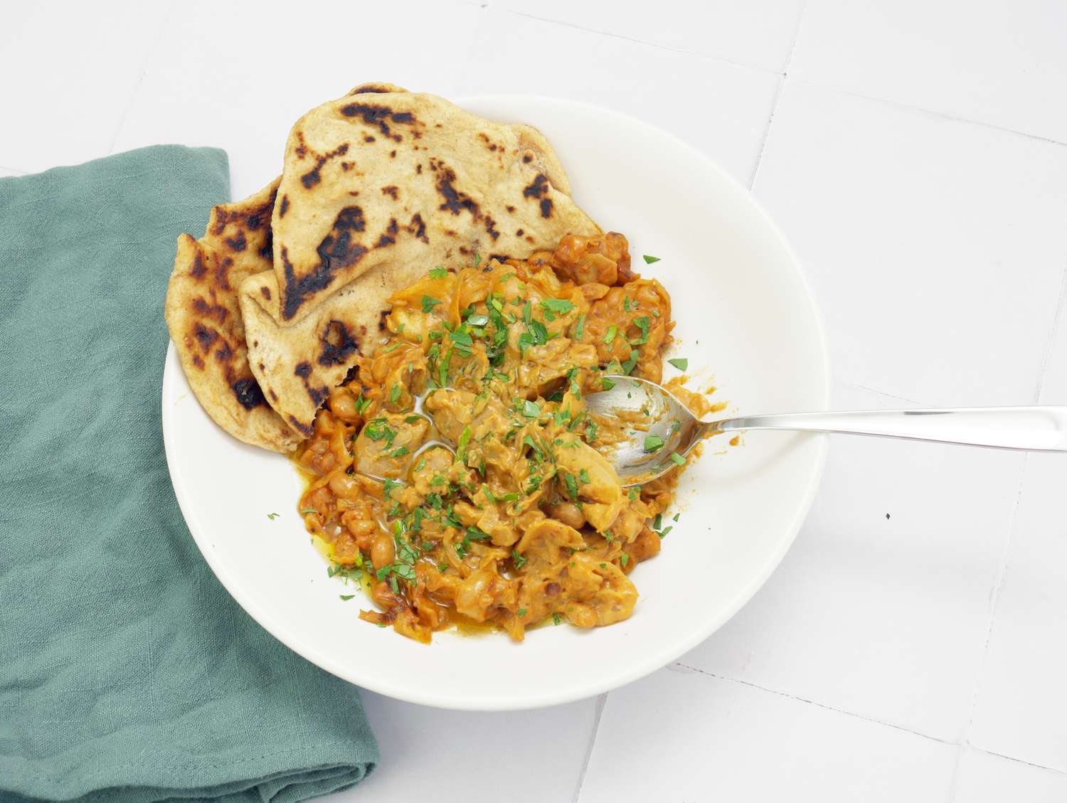 A bowl of food with flatbread garnished and served with a spoon